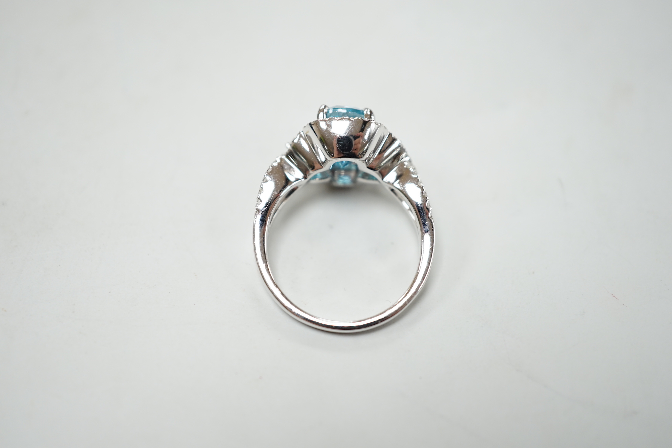 A modern 14k white metal, cushion cut blue zircon and diamond chip set cluster dress ring, with diamond chip set shoulders, size O, gross weight 6.8 grams.